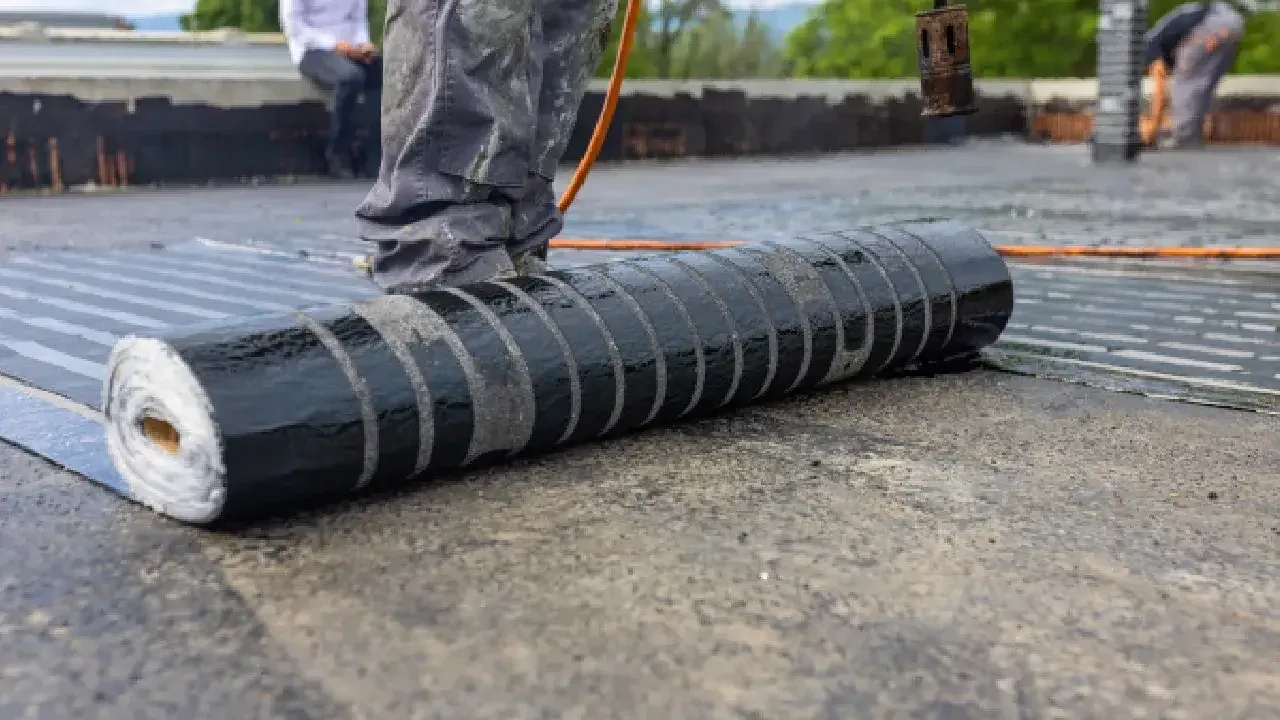 Roofing crew unrolling a torch-applied modified bitumen membrane on a flat roof